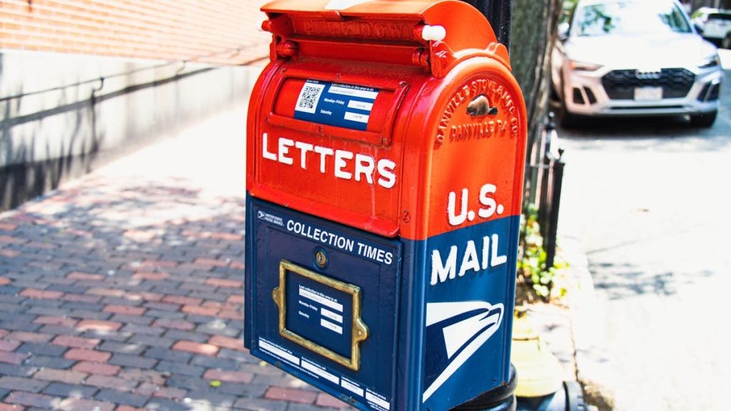 Vibrant U.S. mailbox on a city sidewalk with a parked car, conveying a classic urban scene.