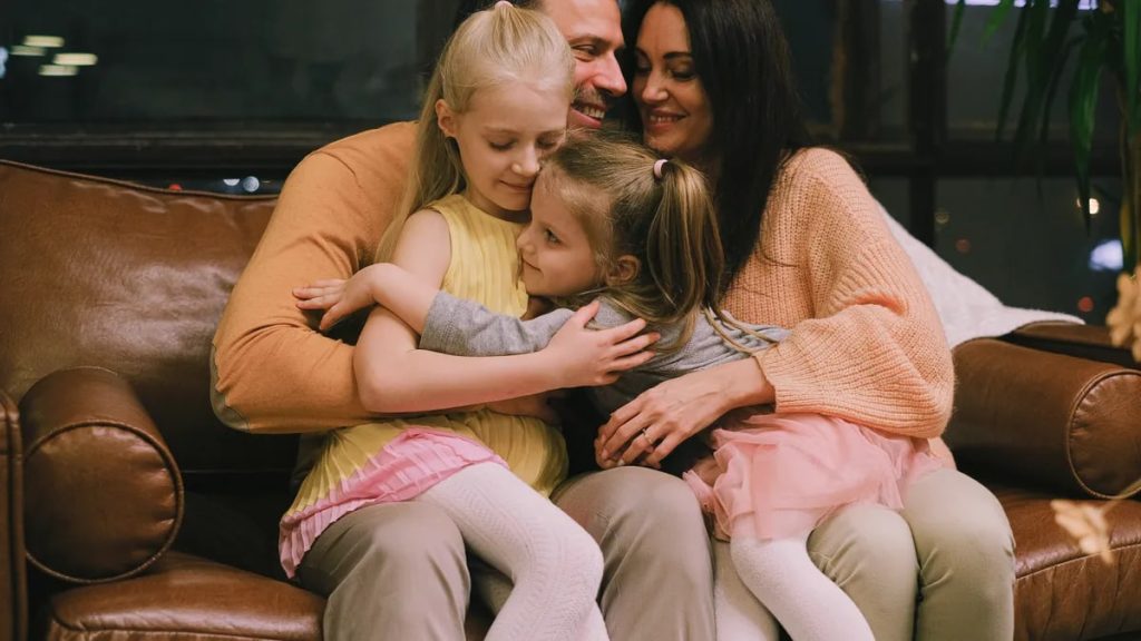 A joyful family shares a warm embrace on a comfortable leather sofa at home.